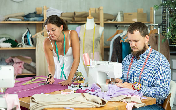 istock Tailor sewing with colleague cutting fabric in modern studio 2231413683