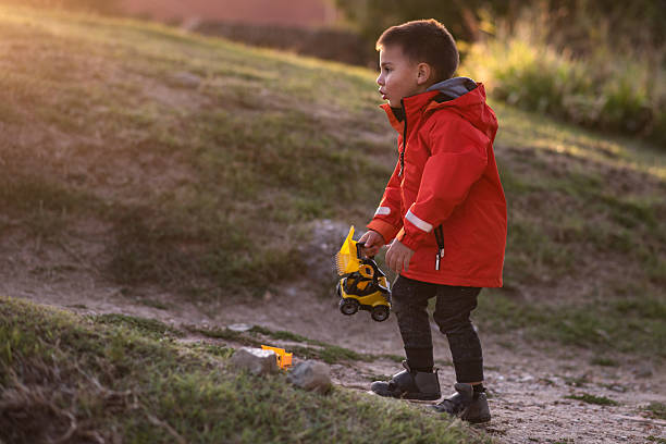 Young boy enjoying outdoor playtime with toy trucks in a natural setting, bathed in the warm glow of the setting sun