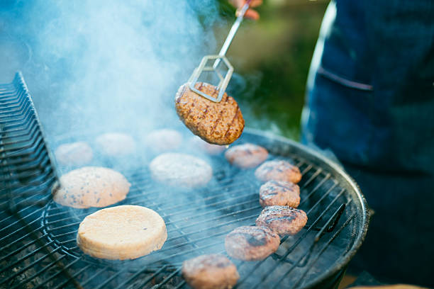 Close-up of woman preparing burgers on a BBQ grill at the front yard.