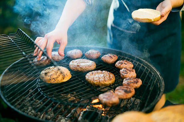 Close-up of woman preparing burgers on a BBQ grill at the front yard.