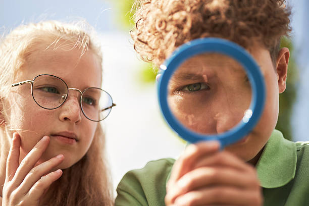 istock Caucasian Girl and Caucasian Boy Examining Object Outdoors Using Magnifying Glass 2231415658