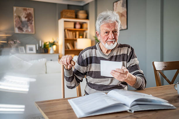istock Senior man reading mail and holding walking stick at home 2231420676