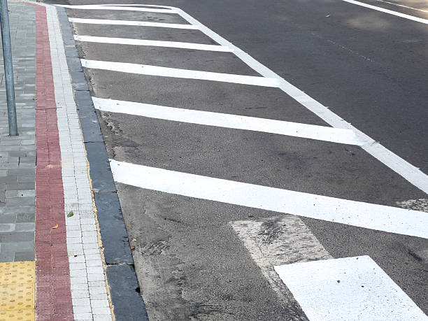 istock White painted lines create a crosswalk on a city street, with adjacent sidewalks visible and a clear sunny sky above 2231422720