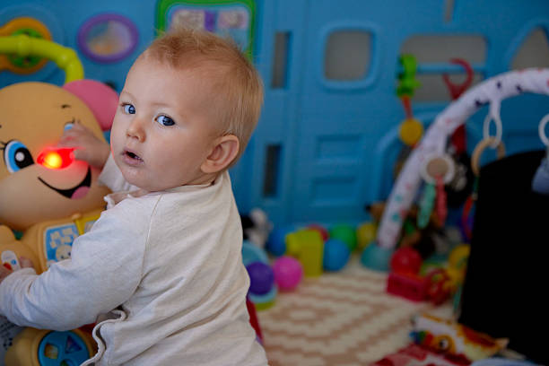 A happy baby sits in a playpen, actively playing with toys. The scene is full of natural movement, curiosity, and joyful interaction in a safe and comfortable environment.
