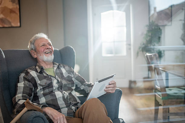 istock Senior man relaxing in armchair, using digital tablet and laughing 2231430615