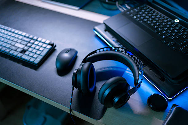 Modern gaming gear setup with laptop, wireless mouse, keyboard and headphone on desktop under cool blue light