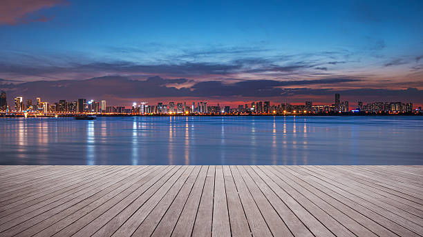 Empty wooden platform and modern urban waterfront skyline with dramatic sky and clouds during sunset