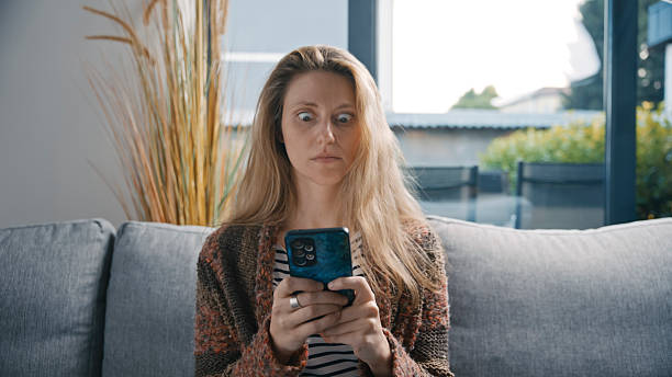 istock Shocked Woman Looking at Smartphone while Sitting on Sofa at Home 2231448290