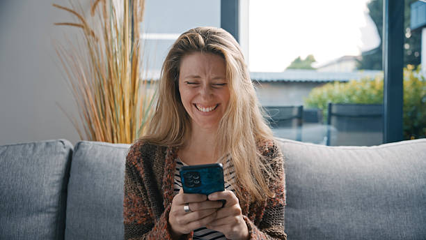 istock Happy Woman Laughing while Using Mobile Phone at Home 2231448492