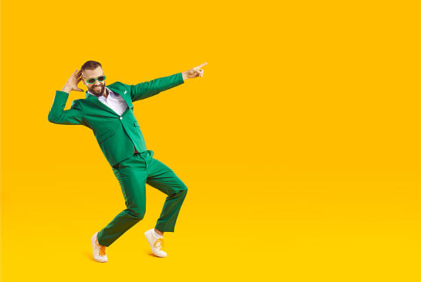 istock Happy funny man in green suit pointing at copy space while dancing on yellow background 2231451968