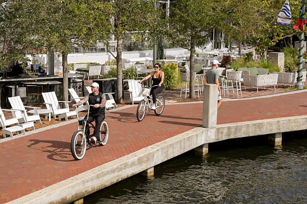 Fort Lauderdale, Florida, USA - 2 December 2023: Two people cycling along the path alongside the river in the city's RiverFront district.