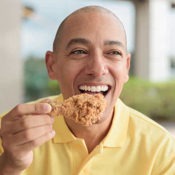 istock Bald Hispanic man eating fried chicken for lunch during day outdoors close-up shot 2231464208