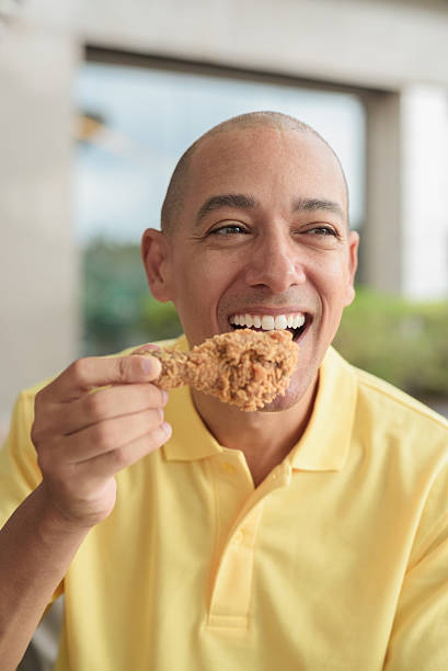 istock Bald Hispanic man eating fried chicken for lunch during day outdoors close-up shot 2231464258
