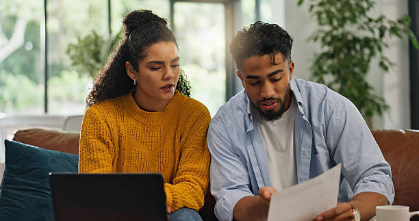 istock Financial analysis, home and couple with documents, talking or discussion with information or bills. Asset management, online and people with paperwork in living room, laptop and planning in house 2231464640