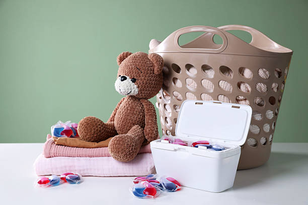 istock Detergent capsules, clean linens, teddy bear and laundry basket on white table 2231466028
