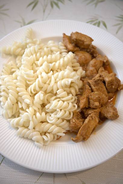 Traditional Hungarian chicken stew served with homemade pasta on white plate, close-up.