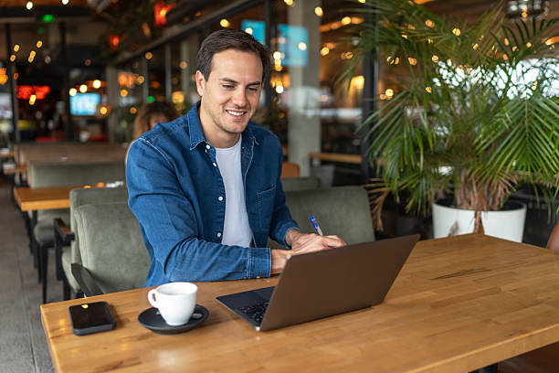 istock Young businessman working on his laptop at a cafe, taking notes and smiling 2231470288