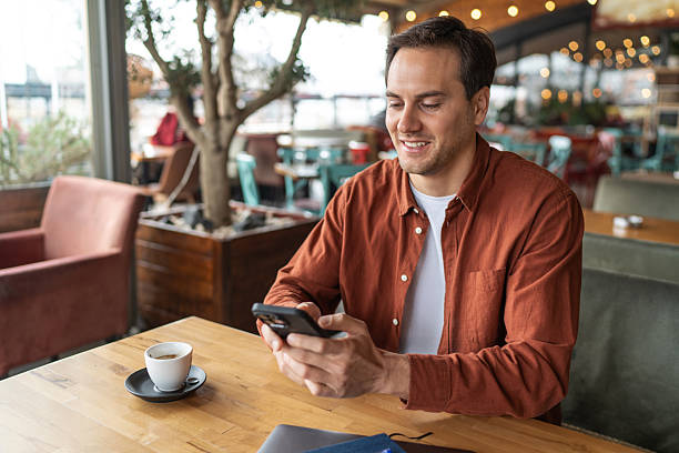istock Young adult man using smartphone and drinking coffee in cafe 2231472305