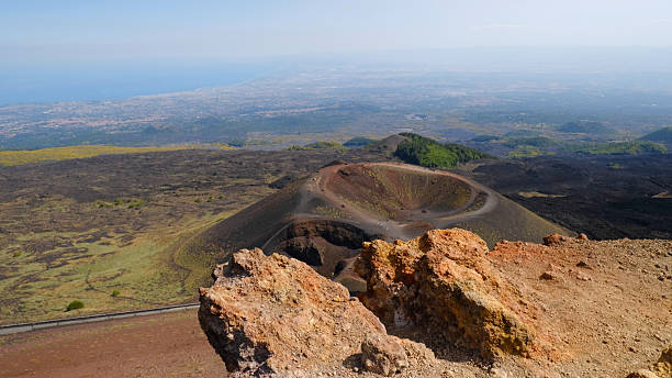 istock Rugged volcanic landscape with large, rust-colored rock, and cinder cone and volcanic crater. Powerful beauty of volcanic region, unique environment of Mount Etna. Travel, nature, geology. 2231476321