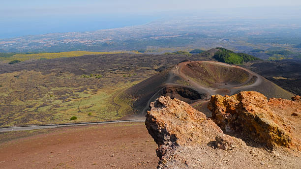 istock Rugged volcanic landscape with large, rust-colored rock, and cinder cone and volcanic crater. Powerful beauty of volcanic region, unique environment of Mount Etna. Travel, nature, geology. 2231476328