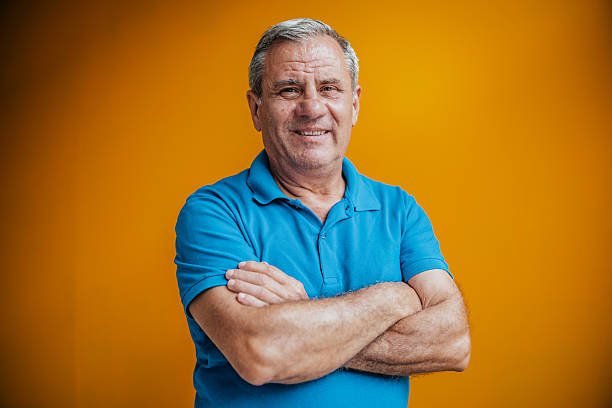 istock Senior man with a cheerful expression poses against a vibrant yellow background in a studio setting 2231477012