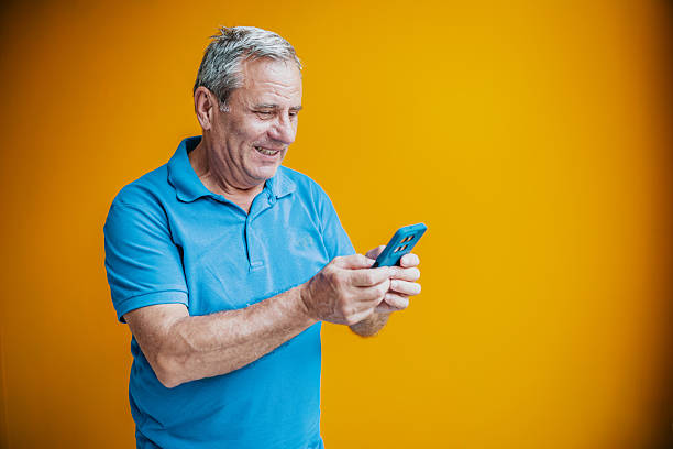 istock Senior man smiling while using smartphone against a bright yellow background in a studio setting 2231478110