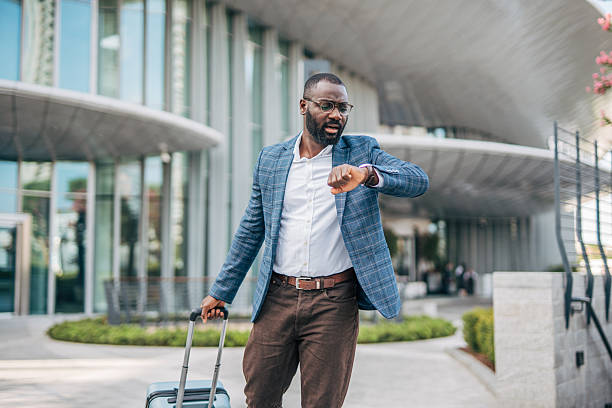 istock Businessman checking time while walking with luggage outside modern building 2231478140