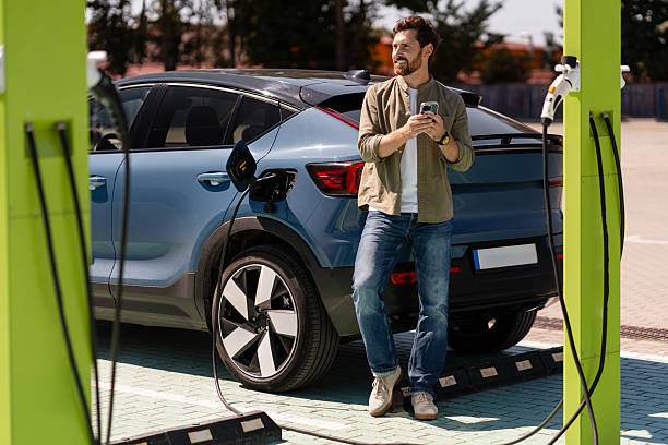 istock Man charging electric car and using smartphone at charging station 2231478147