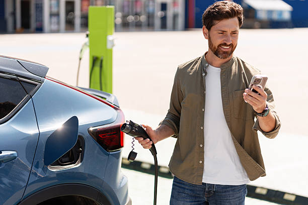 istock Man charging electric car and using smartphone 2231478274
