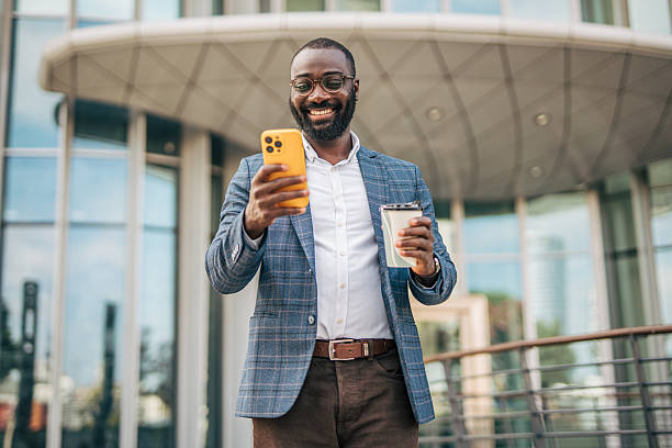 istock Smiling businessman using smartphone and holding coffee outside office 2231478366