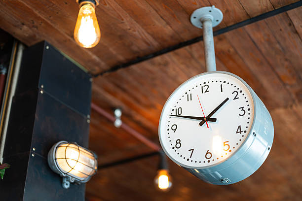 A classic style ceiling round clock which is pointing in the afternoon time, that installed on the wooden ceiling. Interior decoration object photo, close-up.
