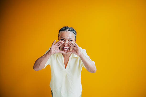 Senior woman with joyful expression on yellow background engaging in cheerful communication indoors