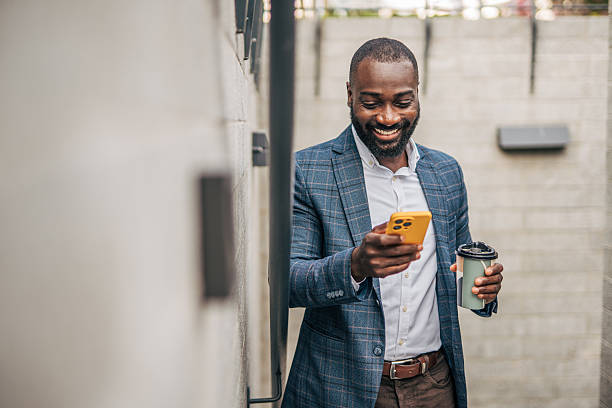 istock Smiling businessman using smartphone and holding coffee outside office building 2231479211