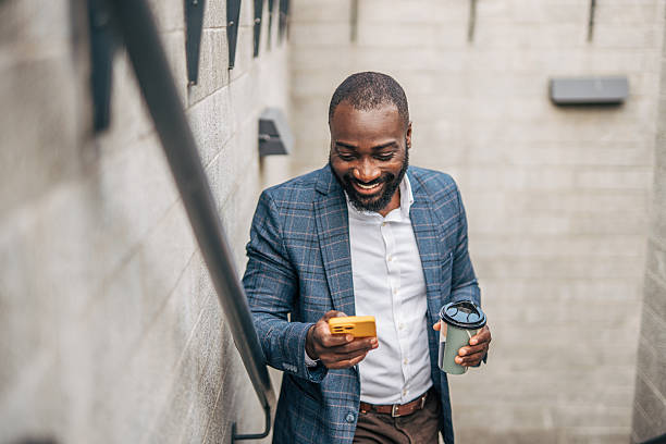 istock Smiling businessman using smartphone and holding coffee walking down stairs 2231479241