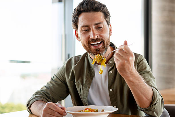 istock Man eating pasta with pesto and smiling at restaurant 2231479774