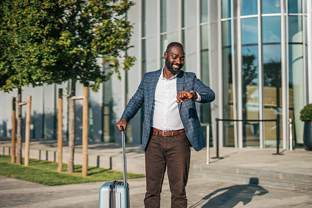 istock Businessman checking time while walking with luggage outside modern building 2231480072
