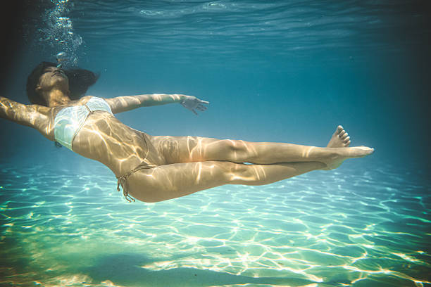 istock Female Swimmer Moving Slowly Beneath Surface Surrounded By Bright Sun Rays And Crystal Clear Waters 2231480427