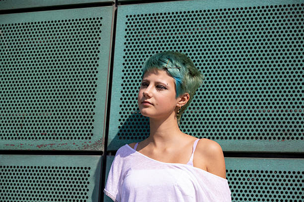 A woman with dreadlocks is standing in front of a green wall. She appears confident and stylish, showcasing her unique hairstyle.