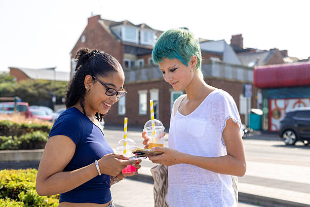 A medium shot of two female teenage friends transferring money to each other via their mobile phones. They are hanging out together with colourful refreshments and striped straws. They are holding their mobile phones together while transferring the money.Videos are available similar to this scenario.