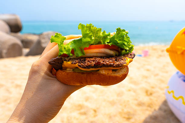 Woman holding burger in a hand against beach background