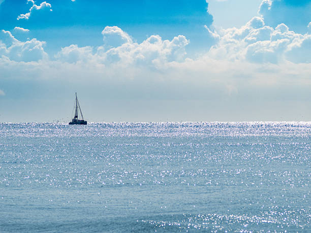 Sailboat on the sea under a blue sky with scattered clouds, illuminated by sunlight with reflections on the water