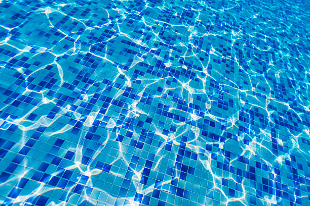 A close-up image of blue ceramic tiles at the bottom of a swimming pool. The surface distortion caused by the water creates a wavy and abstract visual effect, highlighting the dynamic interplay of light and water. Ideal for backgrounds, design concepts, or visuals related to summer, relaxation, or aquatic themes.