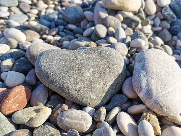 A heart shape made from smooth pebbles rests on the sand at the beach, showcasing an artistic touch in a natural setting.
