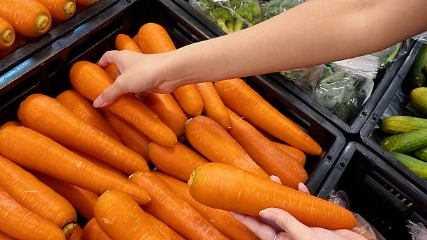 A person is holding a carrot in a grocery store
