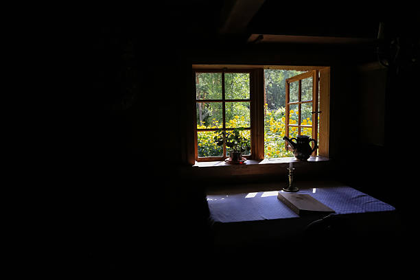 Open window in the old wooden house with summer garden .Sunlight , the table covered with white tablecloth , candle and kettle. Black background.