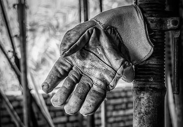 A worn-out work glove hanging on a metal structure, showcasing its texture and details in black and white