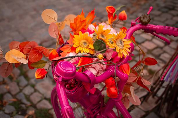 A decorated pink bicycle features sunflowers, red and orange foliage, and greenery, evoking seasonal warmth and vintage charm.