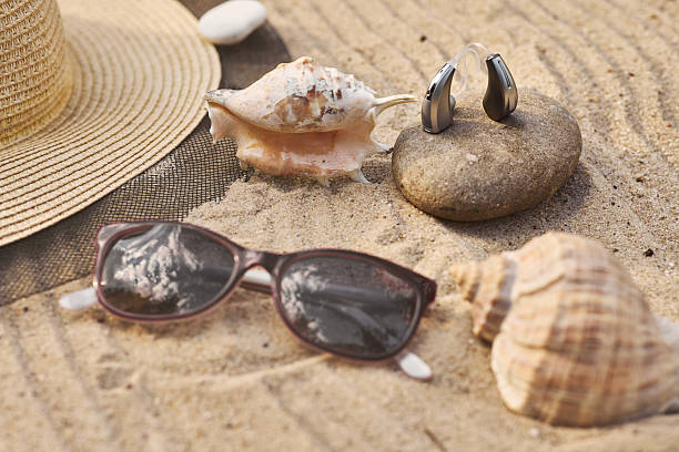 istock Hearing aid sits on a smooth stone alongside seashells and stylish sunglasses in a sunlit sandy beach on vacation 2231517487