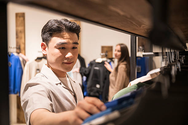 istock Young Korean man looking at clothes on railing inside retail mall 2231518921
