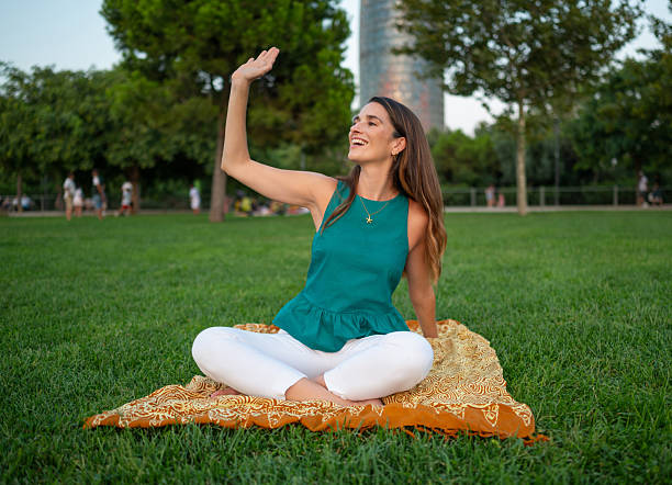istock Happy young woman waving while sitting on blanket in park 2231531731